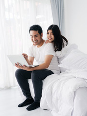 Happy Asian couple using laptop on bed together at home, lifestyle concept.