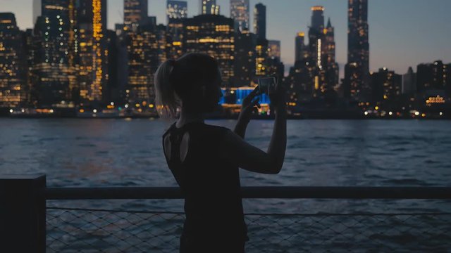 Attractive mid-30s Caucasian taking pictures of Manhattan Downtown with her phone in the evening. 4K UHD