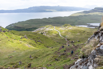 Fototapeta na wymiar Steinfels im Vordergrund, Berg fällt ab auf dem Weg laufen vereinzelt Leute unten das Meer mit Inseln 