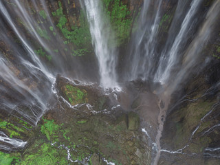 Close-up drone view of water gushing over the edge of a moss and plant covered cliff at Coban Sewu in Java, Indonesia