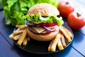 Tasty fresh closeup burger and french fries on wooden table. Homemade hamburger with fresh vegetables.