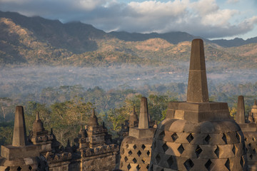 Fototapeta premium Fog covers the lower grounds with views from Borobudur Temple after sunrise in East Java, Indonesia