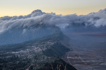 Sunrise and clouds rolling over the caldera rim of Mount Bromo with a view of Cemoro Lawang village in East Java, Indonesia