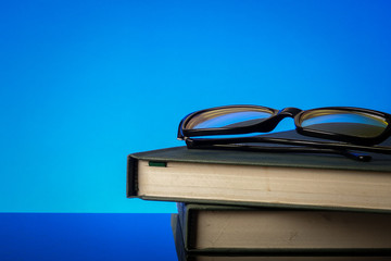 EDUCATION CONCEPT with stack of old book and reading glasses on a blue background.