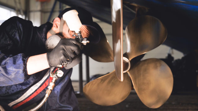 The yacht technician cleans the propeller using a chemical spray (paint) cleaner from dirt. Concept from: New technique, Chemistry, Profesional, Paint, Respirator, Mask, Yacht Club.	
