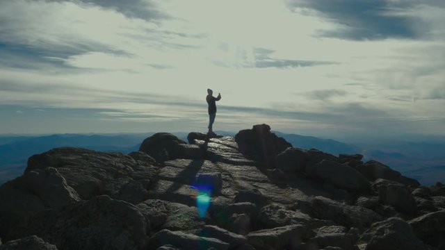 Caucasian mid 30s female standing on a cliff, taking pictures of a mountain valley with her phone. 4K UHD