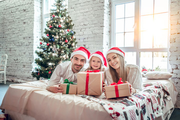 Family in Christmas Santa hats lying on bed.