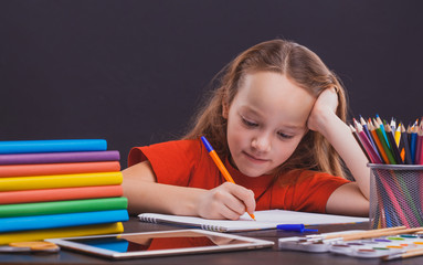 Back to school. Cute child is sitting at a desk indoors. Kid is learning in class on background of blackboard.