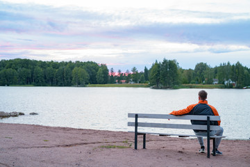 Naklejka na ściany i meble Young Man Sitting On The Bench By The Lake