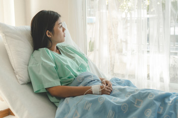 young woman sitting on the bed and looking outside window in hospital worry about her illness. - Powered by Adobe