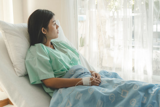 young woman sitting on the bed and looking outside window in hospital worry about her illness.