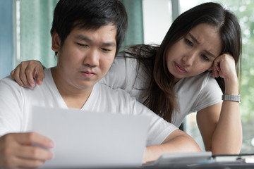 Family financial crisis. Stressed young asian couple looking at issues notification from bank about late payment home loan credit.