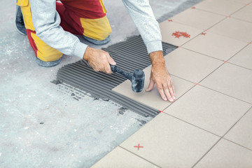 Ceramic Tiles. Tiler placing ceramic floor tile in position over adhesive.