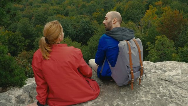JIB SHOT Male mid 30s hiker couple relaxing on a cliff, enjoying the view of a valley. 4K UHD