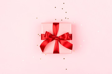 Pink gift box with red bow on the pink background with sparkles. Holiday concept.