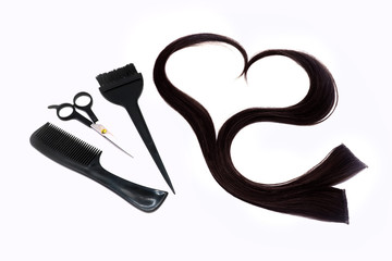 a strand of black hair in the shape of a heart, brushes, scissors and comb , hairdressing tools on a white background, isolated