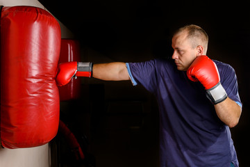 novice male boxer training with punching bag on dark background.