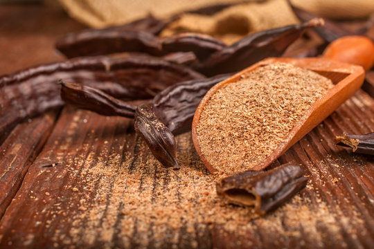 Carob pods and carob powder in a spoon on rustic background
