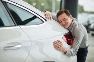 Foto op Canvas Close up of adult content caucasian man being completely satisfied with his new car, hugging it with eyes closed and leaning on car bonnet © alfa27