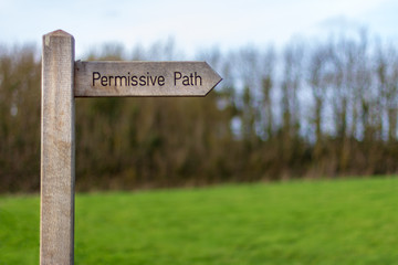A wood trail sign points the way of the "Permissive Path" with trees and a meadow in the background