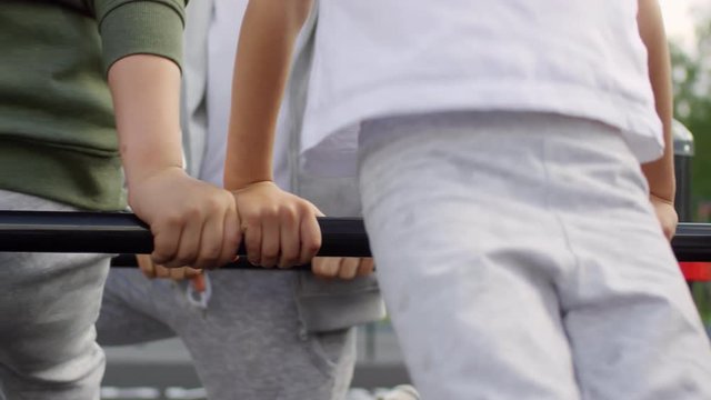 Close-up mid-section shot of unrecognizable children doing squats by bar on outdoor workout playground while training with parents