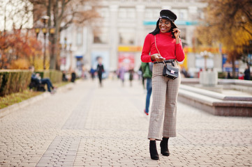 African american fashion girl in newsboy cap and handbag posed at street.
