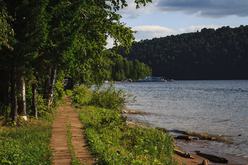 Walk path along the shore and under trees on sunny summer day, in Russia, Pavlovsk reservoir