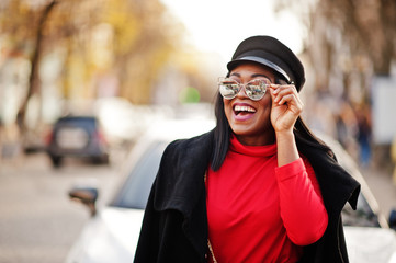 African american fashion girl in coat, newsboy cap and sunglasses posed at street against white business car.