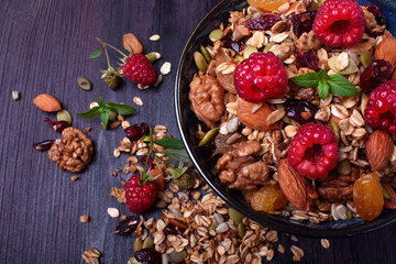 Granola made of oatmeal flakes, nuts and seeds decorated with big raspberries against the dark background