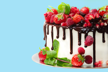white cake poured with brown chocolate and decorated with berries on an isolated blue background