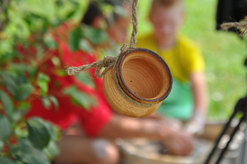 Clay pot hanging on a rope. In the background blurred Potter teaches the child to sculpt a pot on a Potter's wheel