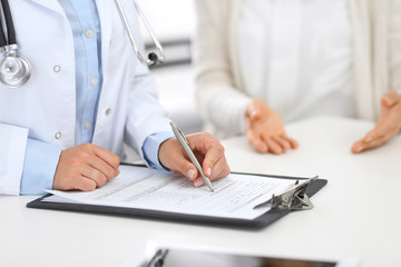 Fototapeta premium Unknown doctor and female patient discussing something while standing near reception desk in emergency hospital. Physician at work in clinic. Medicine and health care concept
