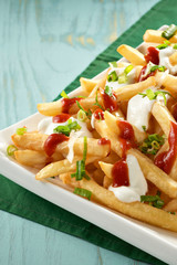 Dish of delicious french fries with ketchup and mayonnaise, on top of a green napkin on blue wooden table
