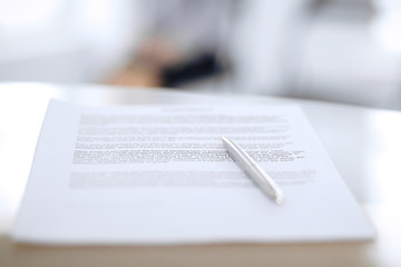 Obraz premium Contract with a pen and blurred business people on the background, close-up