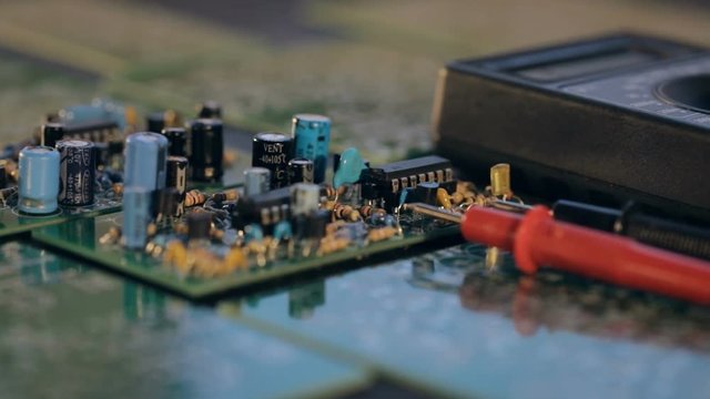 Panoramic shot over circuit boards with electronic details and a multimeter on a black table