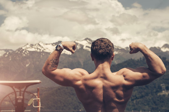 Young bodybuilder showing muscles shape outdoors, Handsome muscular bearded man looking at highlands landscape with foggy sky from the peak of the mountain, feeling hapyness and joy.