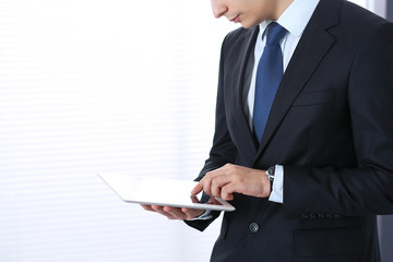 Young businessman using tablet computer while standing straight in office. Business concept