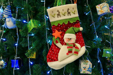 Snowman Christmas Sock with Many of Vibrant Colored Gift Box Ornaments Hanging on a Sparkling Christmas Tree