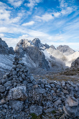 Mountain peaks with a stone wall and rocks in the foreground and snow on their tops under a blue sky, Tyrol, Austria