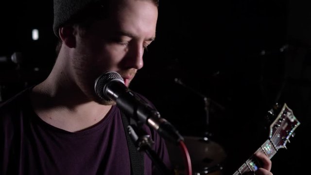 A man plays an electric guitar and sings in a dark room. 4K Average plan.