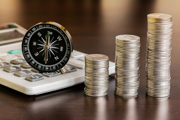 Stack of coins with calculator and compass on wood table