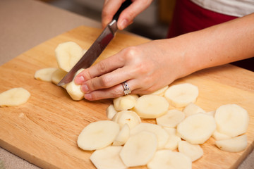 Fototapeta na wymiar Young Woman Cutting Potatoes in Kitchen at Home