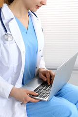 Woman doctor typing on laptop computer while working in hospital office, close-up. Data in medicine and health care