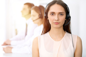 Call center operators. Focus on young cheerful smiling woman in headset. Business and customer service concepts