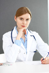 Doctor woman filling up prescription or medical record form while  sitting near window in clinic or hospital. Medicine and healthcare concept. Physician at work