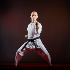 On dark background athlete doing formal karate exercises.