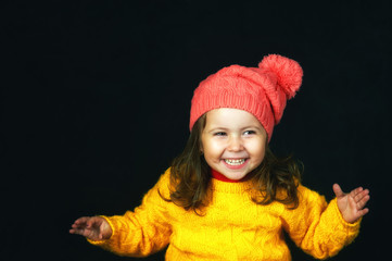 Close-up portrait of a little cheerful girl on a dark background . The child is dressed in a bright yellow jacket and hat