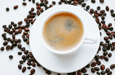 White cup with fresh coffee on saucer close up with grains of coffee on white isolated background