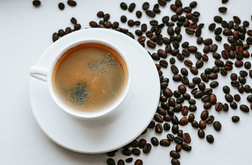 White cup with fresh coffee on saucer close up with grains of coffee on white isolated background