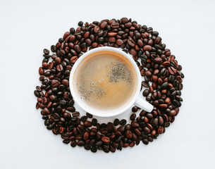 White cup with fresh coffee on saucer close up with grains of coffee on white isolated background